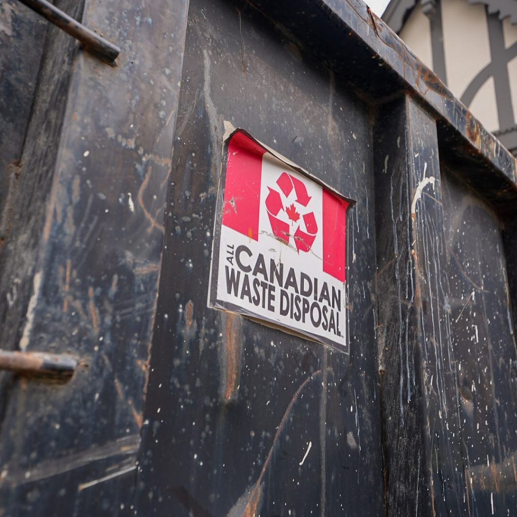 All Canadian Waste Disposal A close-up of a metal dumpster with a sign reading “All Canadian Waste Disposal” and a recycling symbol on a red and white background, showcasing reliable waste management for all your waste bins needs. residential and commercial waste management