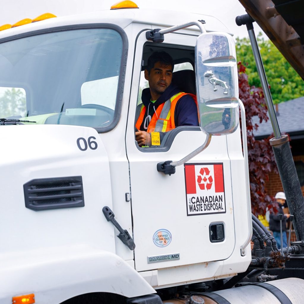 All Canadian Waste Disposal A worker in a safety vest sits in the cab of a white All Canadian Waste Disposal truck, looking out the window, ready to provide top-notch waste management services. residential and commercial waste management